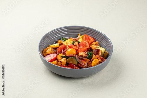 Warm roasted vegetables with tomatoes zucchini and crispy croutons served in gray bowl on light background