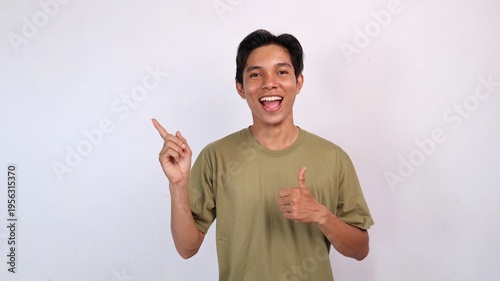 excited young asian man gesturing okay, pointing to the side against white background