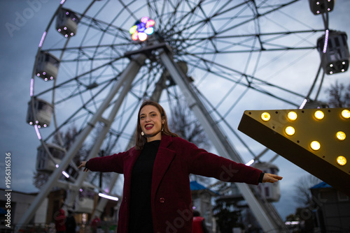 A woman in an amusement park with a Ferris wheel in the background on a summer evening