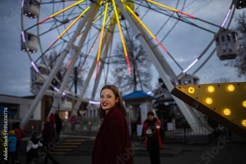 A woman in an amusement park with a Ferris wheel in the background on a summer evening