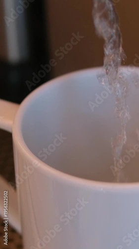 Woman presses a cup of hot water from the water purifier and put it back. Close up look at the glass cup in the kitchen.