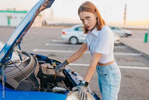 A female driver with an open hood in a parking lot, a car breakdown on the road in summer