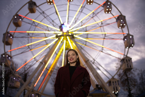 A woman in an amusement park with a Ferris wheel in the background on a summer evening