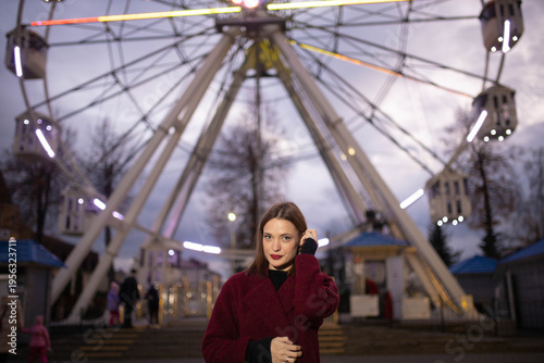 A woman in an amusement park with a Ferris wheel in the background on a summer evening