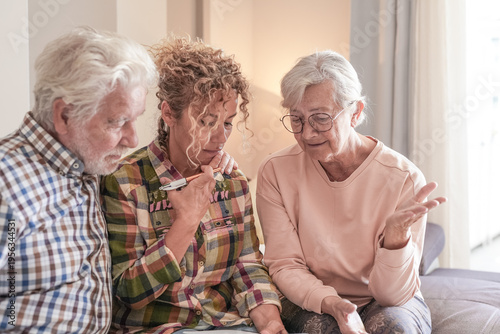 Smiling Senior couple and Caregiver Sharing a Moment sitting together on sofa at home. Concept of assistance and help to our elderly