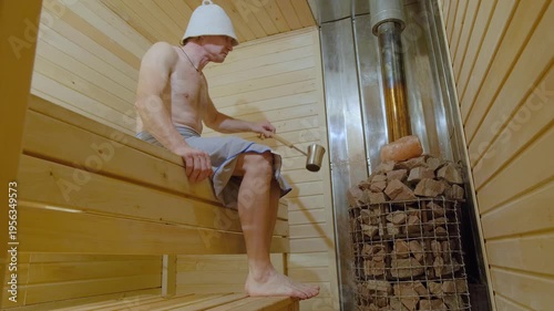 A man relaxes in a sauna and pours water on hot stones.