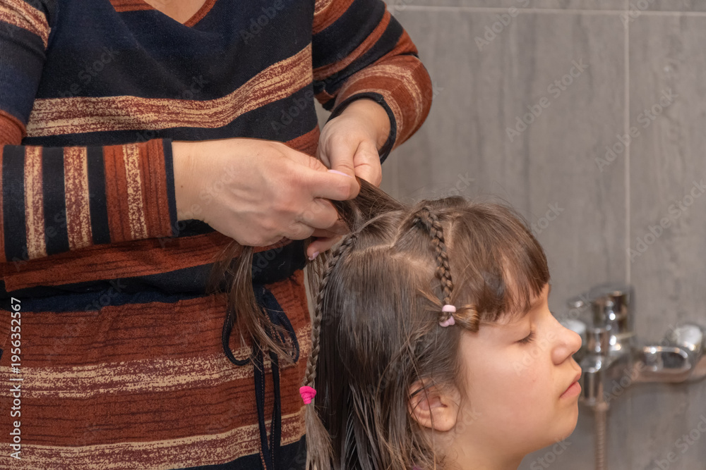 Fototapeta premium Woman's hands carefully interlace strands of girl's hair creating neat hairstyle after washing.