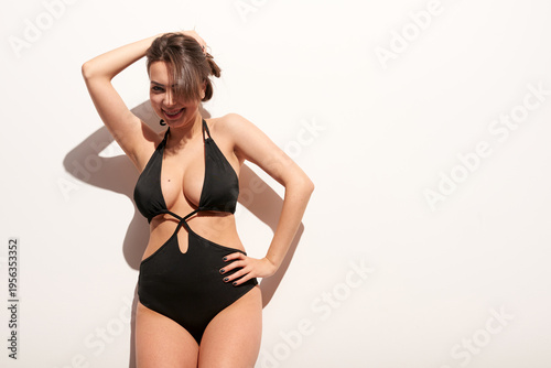 Schilderij op canvas White adult woman in black swimsuit posing in studio with confident smile and hand in hair one person indoor minimal background