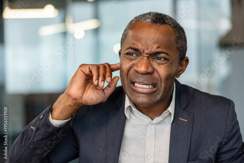 Foto Mature man grimacing, inserting finger into his ear, indicating an irritating no