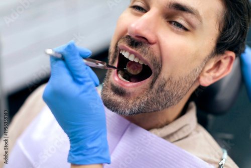 Canvas Print Man patient sitting in dental chair while dentist examining his teeth using dent