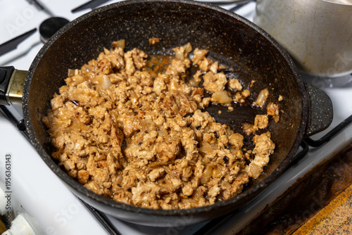 Fried minced meat with onions in frying pan on white stove top