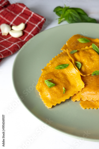 Fresh homemade tomato ravioli with basil and garlic on green plate, Italian cuisine