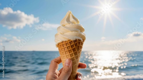 Hand holding creamy vanilla ice cream in waffle cone against sunny seaside with sparkling water and blue sky, representing summer refreshment, leisure, and sweet indulgence.