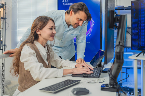 Fotografi female developer in vest codes on laptop while male colleague in blue shirt lean