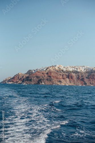 View of Oia village and red volcanic cliffs from a boat on the Aegean Sea, Santorini, Greece.
