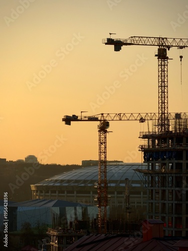 Photography Silhouetted construction cranes and unfinished structures in Moscow, Russia, set against a warm sunset sky