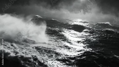 Dramatic monochrome ocean waves in storm with sunlight breaking through dark clouds creates an atmospheric seascape.