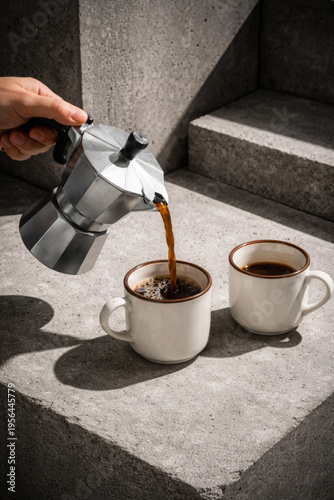 Fresh coffee pouring from moka pot into white ceramic mug on concrete