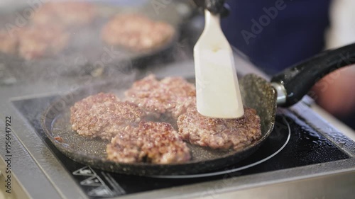 The chef is cooking hamburger patties in a frying pan. Close-up. Very soft focus