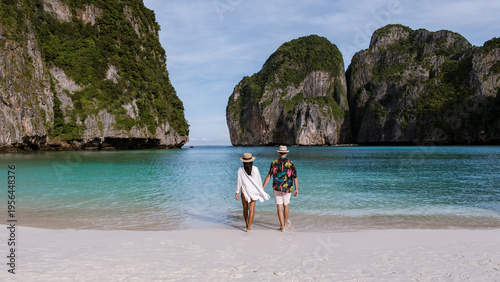 Couples enjoy a tranquil walk on the pristine sandy beach of Koh Phi Phi, surrounded by breathtaking limestone cliffs and crystal-clear waters. Maya Bay, Krabi, Thailand