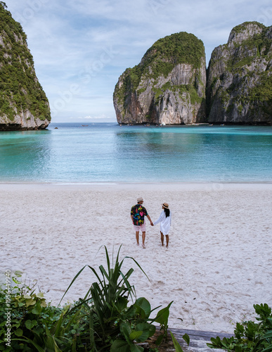 Two travelers stroll along the pristine sandy beach of Koh Phi Phi, Thailand, enjoying the serene atmosphere and breathtaking views of limestone cliffs and turquoise waters at sunset.