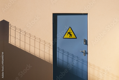 Porte en métal bleue sécurisée par un digicode d'un local technique électrique avec panneau danger électrocution fixé dessus.
