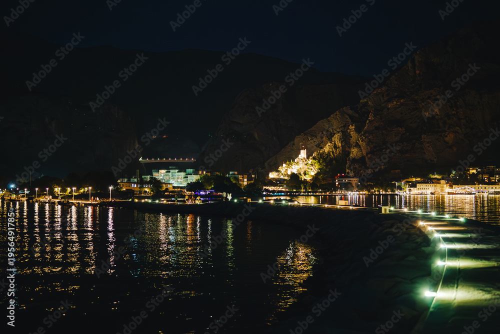 Obraz premium Night view of Omis town and illuminated Mirabella fortress from stone pier.