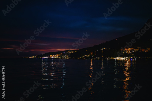 Tableau sur toile Night coastline with city lights and dark sea reflection.