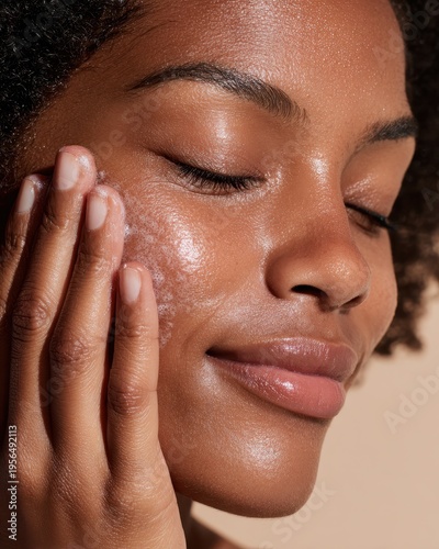 Deep dark skinned woman with eyes closed smiling gently while applying cream on cheek in skincare routine