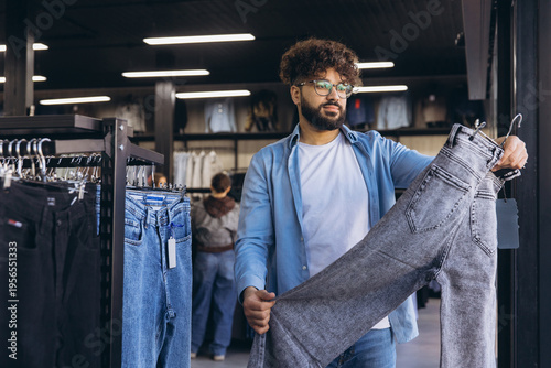 Φωτογραφία Arab man shopping denim jeans at a clothing store, choosing new fashion apparel,