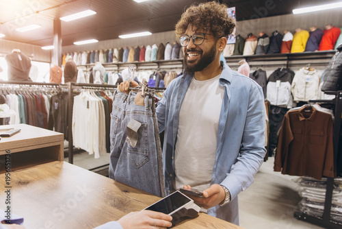Fotografie Arab man paying for new jeans with smartphone using contactless nfc payment syst