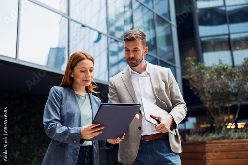 Картината върху платно Businesswoman showing a document to her male colleague in front of a modern office building