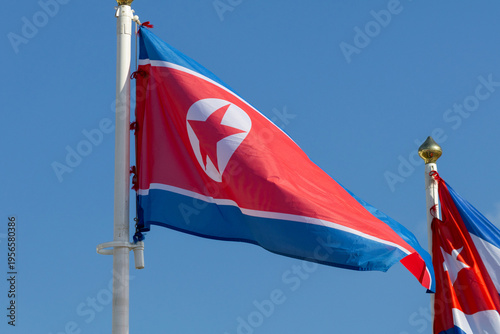 Flag of North Korea (DPRK) and Flag of Cuba Flying Side by Side Against a Clear Blue Sky