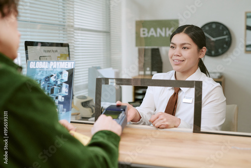 Fotografi Young adult bank teller assisting unseen customer with payment transaction at br