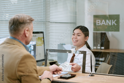 Photos Caucasian middle aged man handing cash to young adult bank teller behind counter