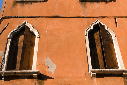 Typical ancient Venetian windows with Gothic arches and dark wooden shutters and stone window sills set into an orange wall. Venice, Italy