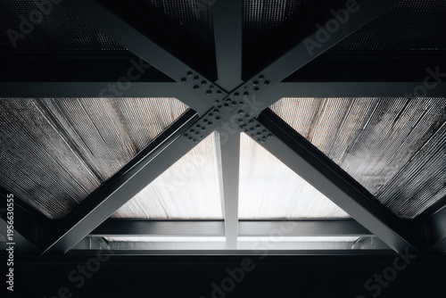 Interior metal structure with cross-shaped black steel beams and mesh panels illuminated by spotlights