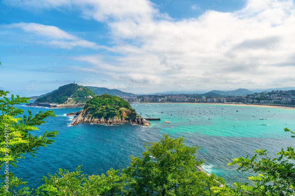 Obraz premium View of Santa Clara Island and La Concha Bay in San Sebastian, with turquoise water, boats and city coastline, Donostia, Basque country, Spain. Coastal landscape representing travel, tourism