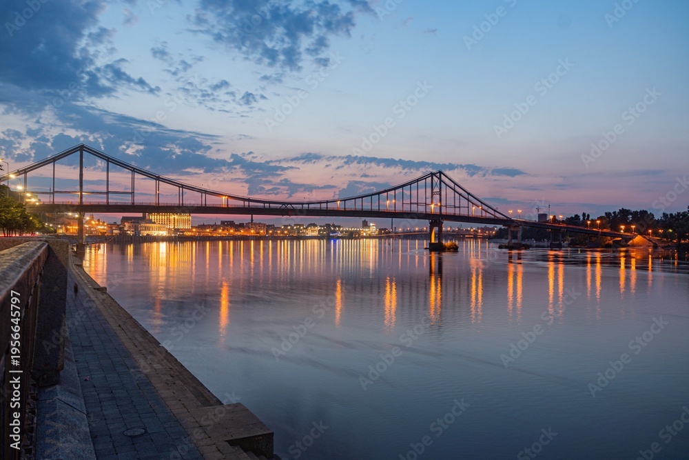 Fototapeta premium Nighttime riverfront scene with illuminated bridge and buildings a