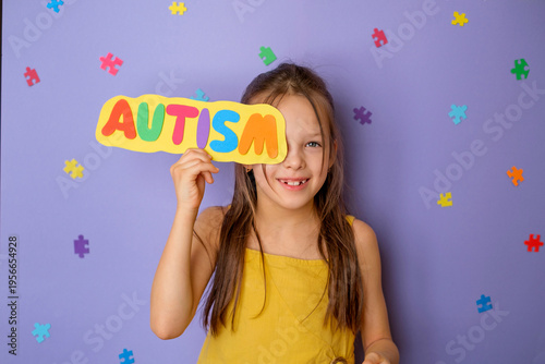 A happy little laughing girl shows a multicolored letter card with the word autism. Awareness and support for people with autism spectrum disorder.