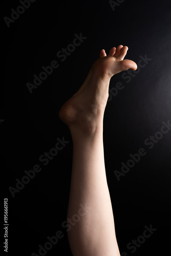 Photos Single raised human leg with bent bare foot against dark background, studio lighting emphasizing contours and skin texture