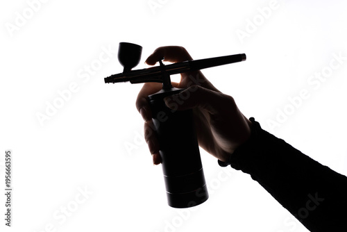 Bild auf Leinwand Human hand holding airbrush with small compressor against white background, studio lighting highlighting tool structure, nozzle, and portable design