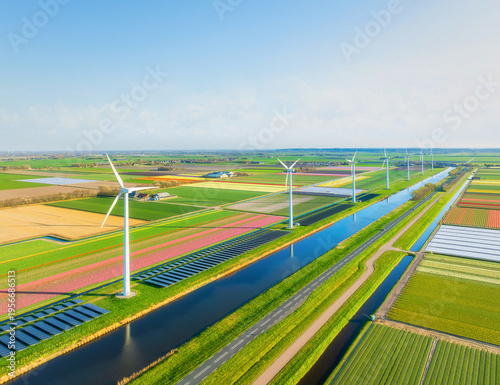 Aerial view of Dutch countryside with wind turbines and solar panels among green fields. Sustainable energy and agriculture in Netherlands under blue sky. Summer sunny day rural landscape from above.