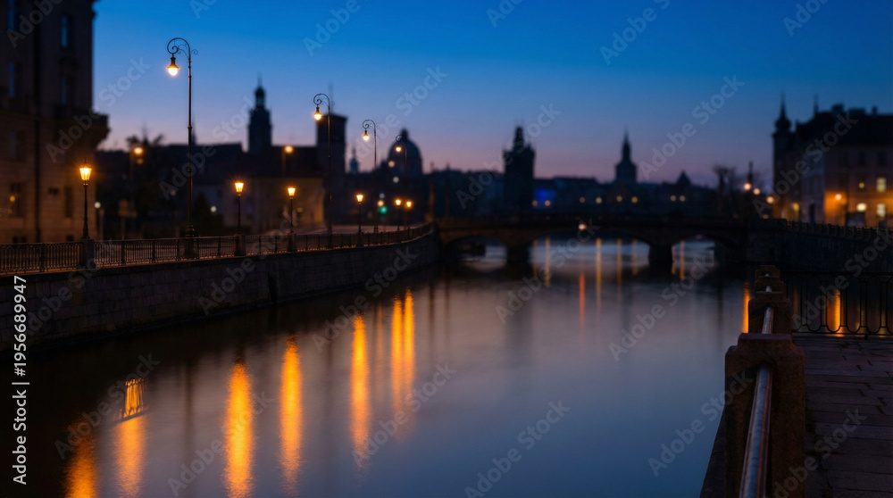 Fototapeta premium Golden City Lights Reflecting on River at Blue Hour Twilight. Warm amber streetlights shimmer across calm water surface during magical blue hour, urban skyline silhouette in soft focus background