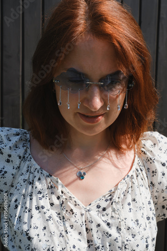 Creative red-haired woman wearing unique cloud-shaped sunglasses with crystal raindrops. concept for sadness, hidden emotions, creativity, or unique fashion.