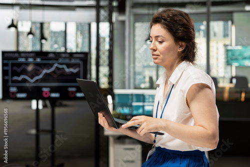 Free Download Female team leader stands in office and analyzes business analytics on laptop. Businesswoman managing company data, preparing reports to boost productivity and success in financial firm. - GFXLoad