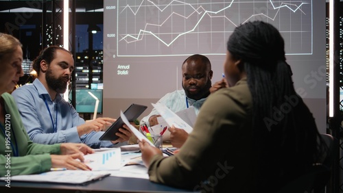 Fényképezés Diverse professionals group evaluating files and performance indicators, using projections and diagrams to align the company objectives with investors expectations for company progress