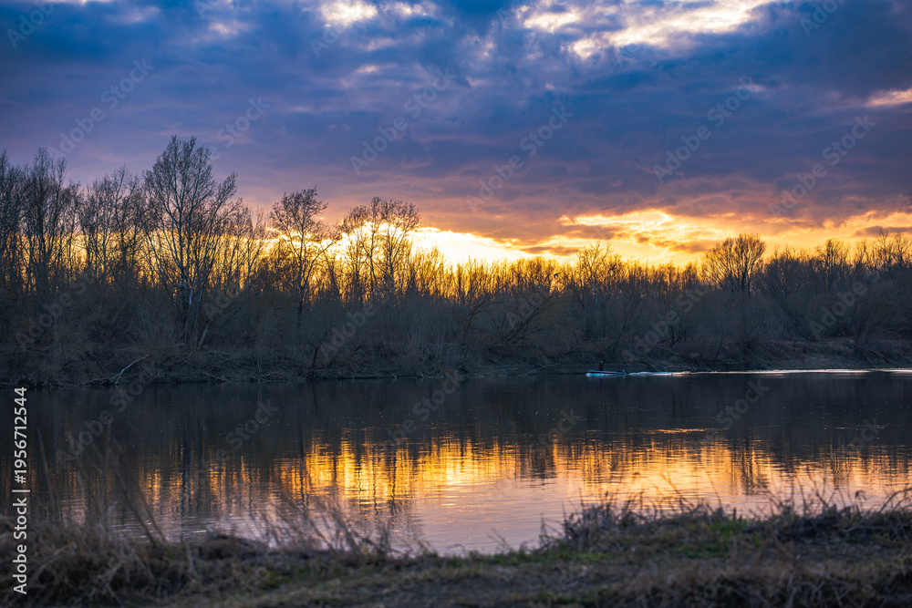 Obraz premium Vistula River near Warsaw at sunset with leafless trees and boat