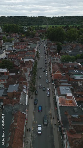 Aerial view of a town street lined with brick buildings, cars, and trees, with a lush forest in the background.