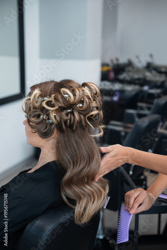 Stylist works on models hair in salon while using rollers to create style for special event